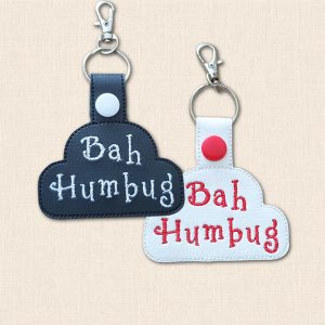 Black and white Bah Humbug embroidered keyrings displayed together, with contrasting lettering, snap-fastened tabs and silver-coloured hardware.