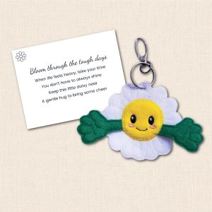Smiling white and yellow felt Daisy Pocket Hug with open green arms beside its printed 'Bloom through the tough days' keepsake verse card.