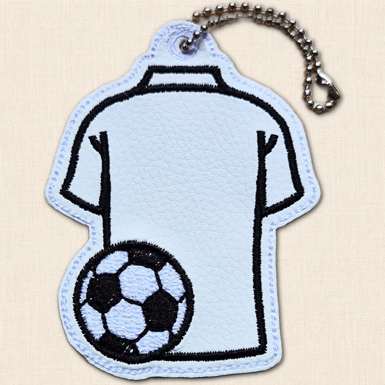 White faux leather football shirt hanging charm with black embroidered shirt outline, football detail and metal ball chain.