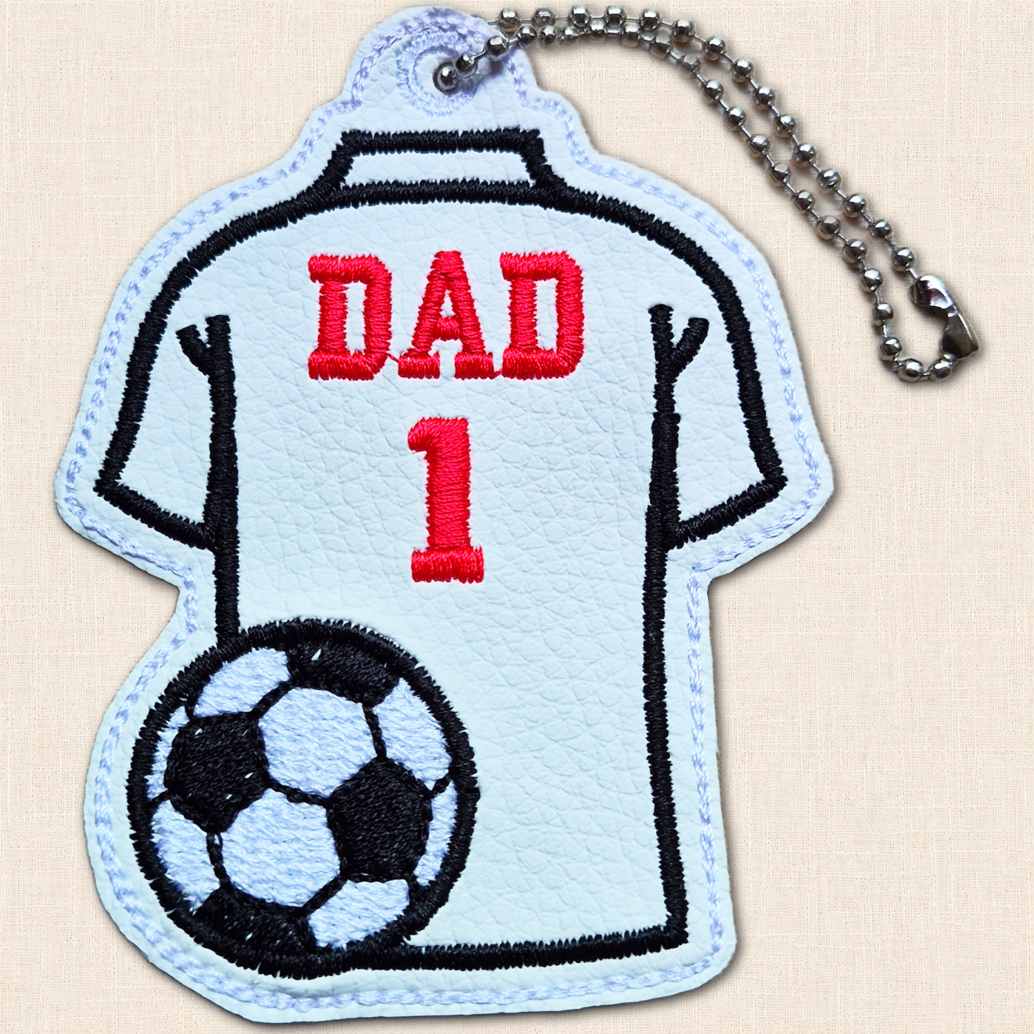 White football shirt hanging charm with red 'Dad' wording and number 1, black football detail and metal ball chain.
