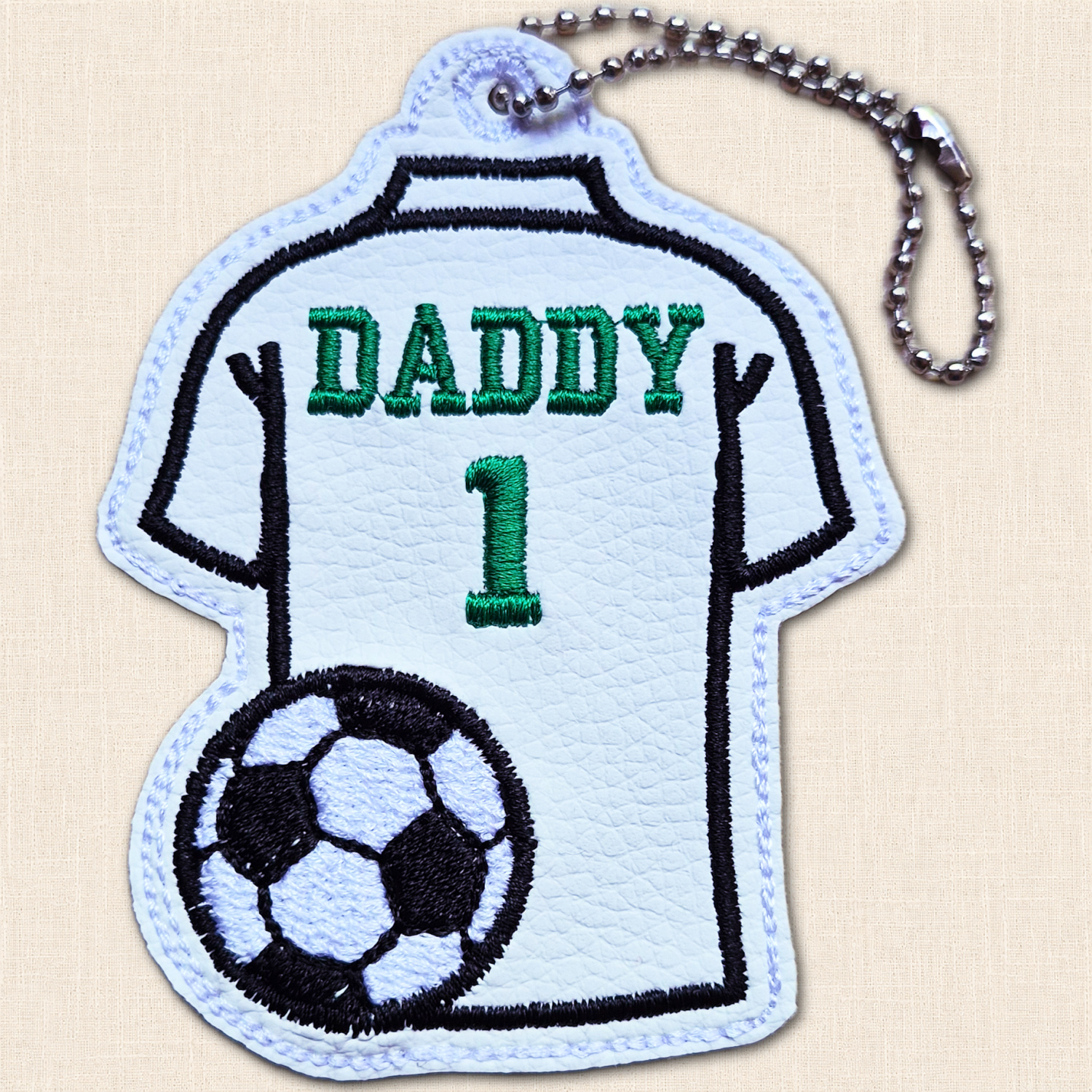 White football shirt hanging charm with green 'Daddy' wording and number 1, black football detail and metal ball chain.