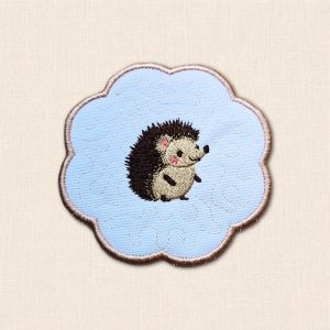 White candle coaster with an embroidered smiling hedgehog, subtle stitched background and beige scalloped border.