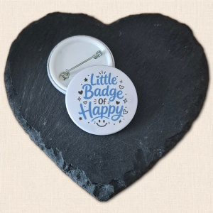 Little Badge of Happy button badge with blue lettering, black hearts, stars and a smiling face on white, alongside a badge showing its pin fastening.