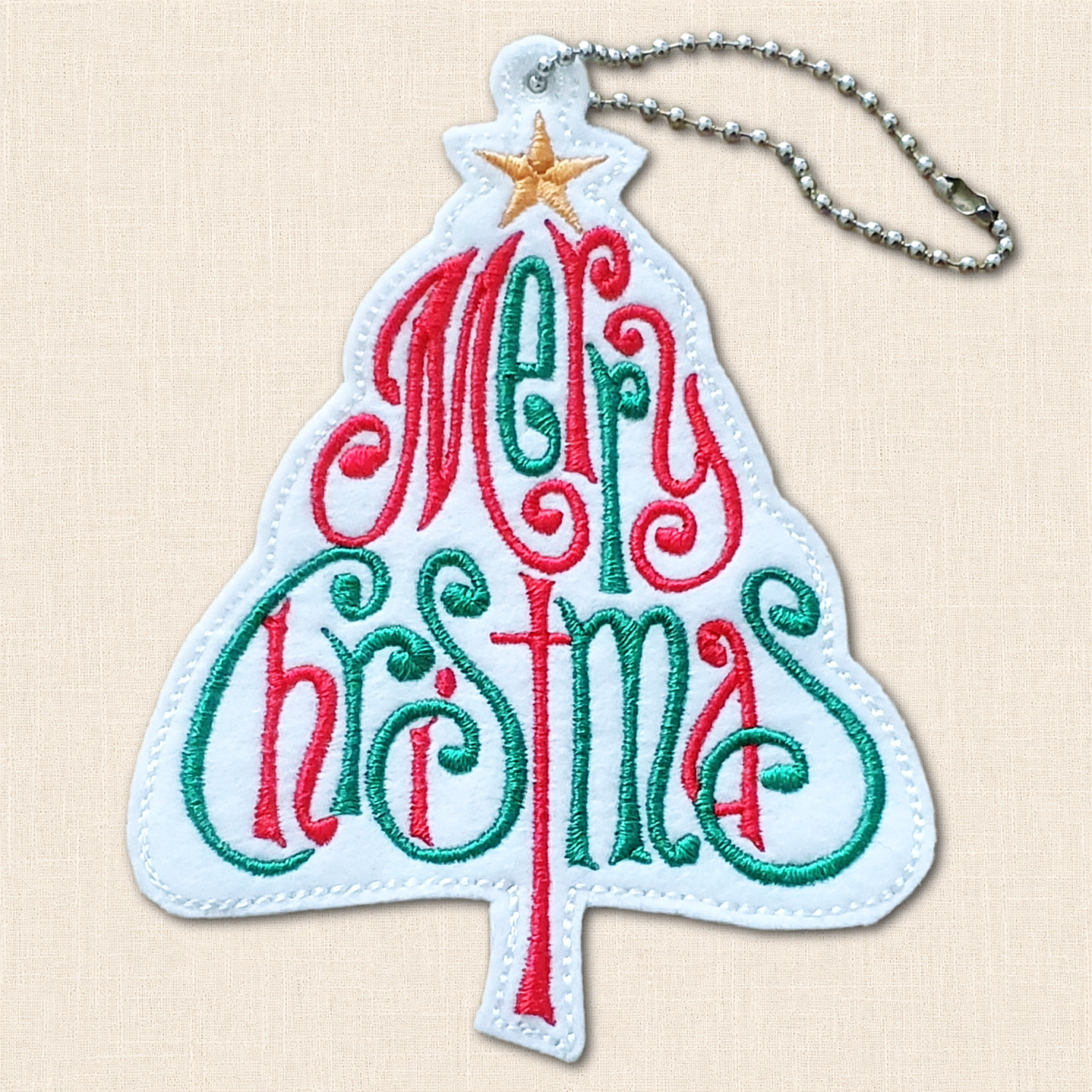 Close-up of flowing red and green 'Merry Christmas' embroidery forming a tree shape, with a golden star and white stitched edging.