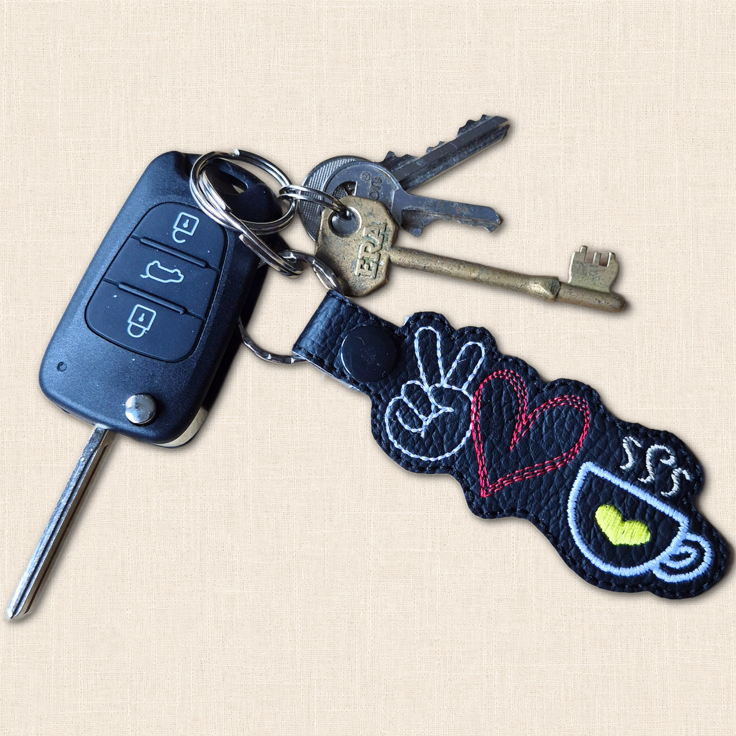 Black peace, love and coffee embroidered keyring attached to a bunch of keys, including a car key, showing its everyday use.