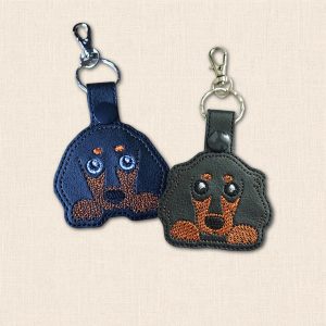 Short haired and long haired Dachshund keyrings side by side, with brown embroidered faces and paws, split rings and lobster clasps.