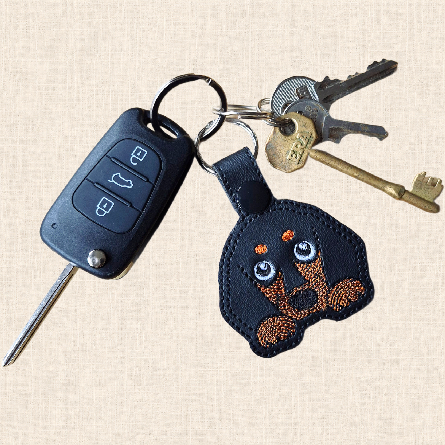 Short haired Dachshund keyring attached to a set of house and car keys on a cream fabric background.
