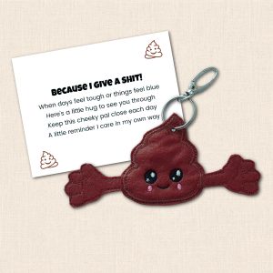 Brown felt Poop Pocket Pal with a smiling face and open arms beside its printed 'BECAUSE I GIVE A SHIT!' support verse card.