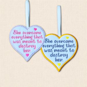 Two felt hearts reading 'She overcame everything that was meant to destroy her', showing purple blanket stitch and golden yellow satin stitch borders.