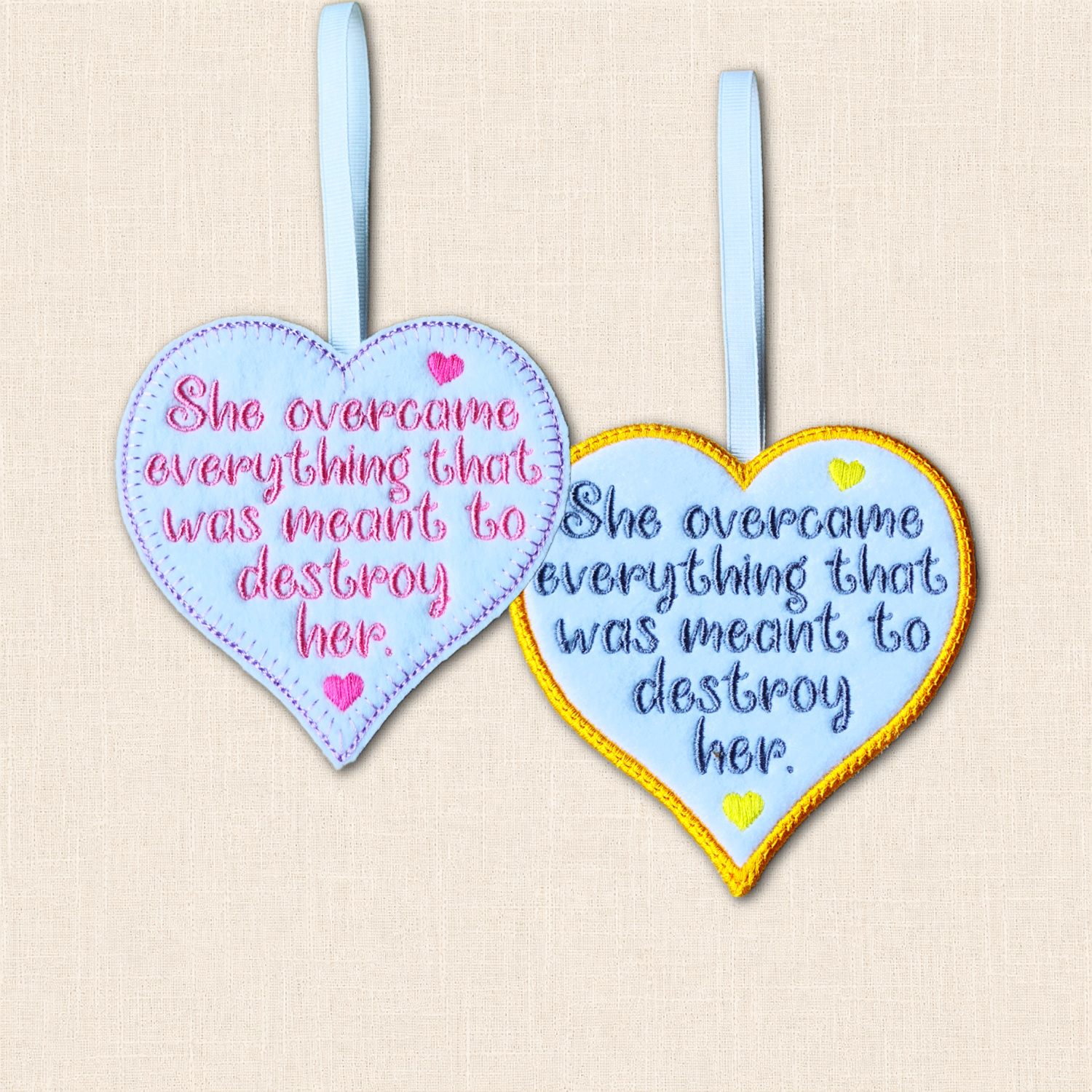 Two felt hearts reading 'She overcame everything that was meant to destroy her', showing purple blanket stitch and golden yellow satin stitch borders.