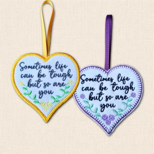 Two felt hearts reading 'Sometimes life can be tough but so are you', with floral embroidery and yellow satin stitch or purple blanket stitch borders.