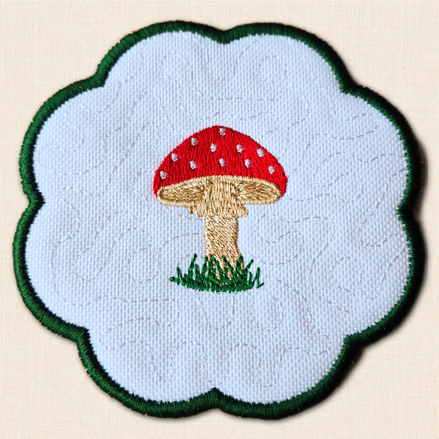 Close-up of a toadstool candle coaster showing the mushroom embroidery, stippled white background and green scalloped border.
