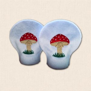 Pair of white felt tealight covers with embroidered red and white spotted toadstools, beige stems and green grass.